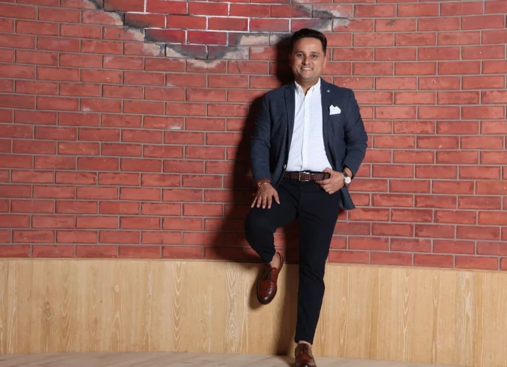 Amish Tripathi standing against an exposed-brick wall